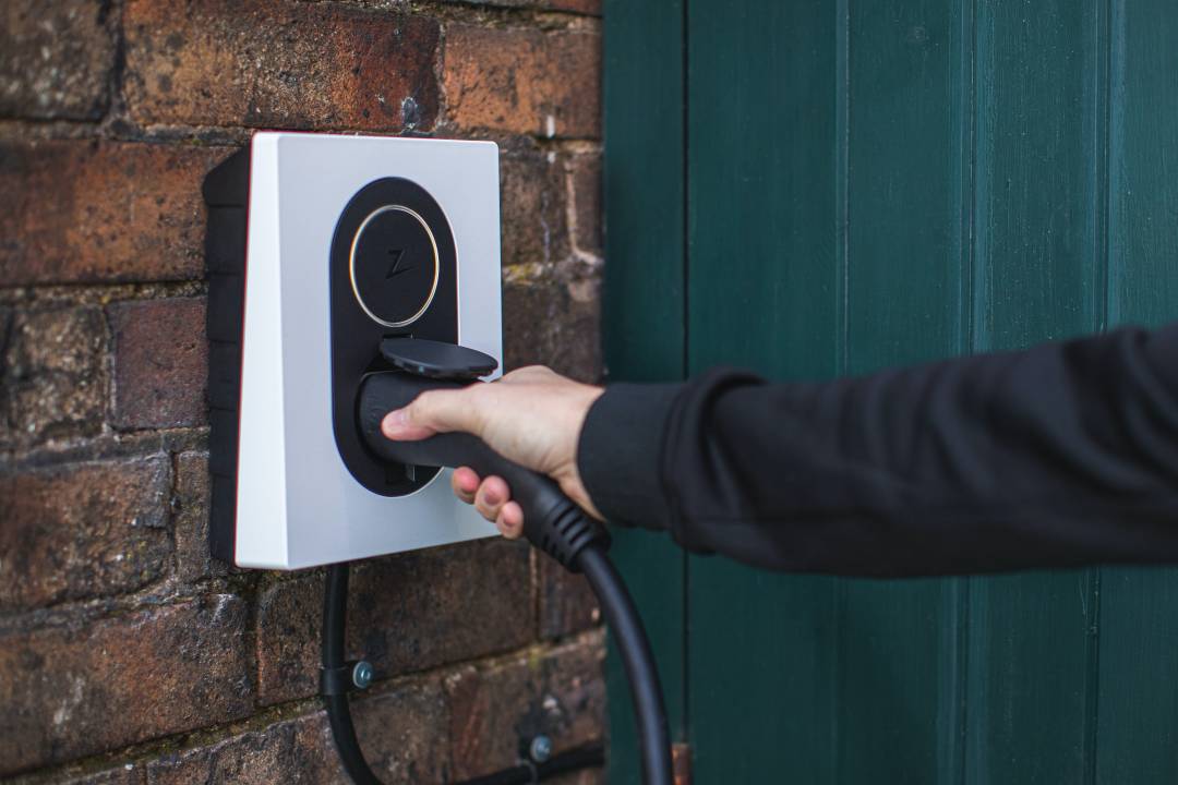 An Electric Charger Mounted To A Wall With A Person Inserting A Plug