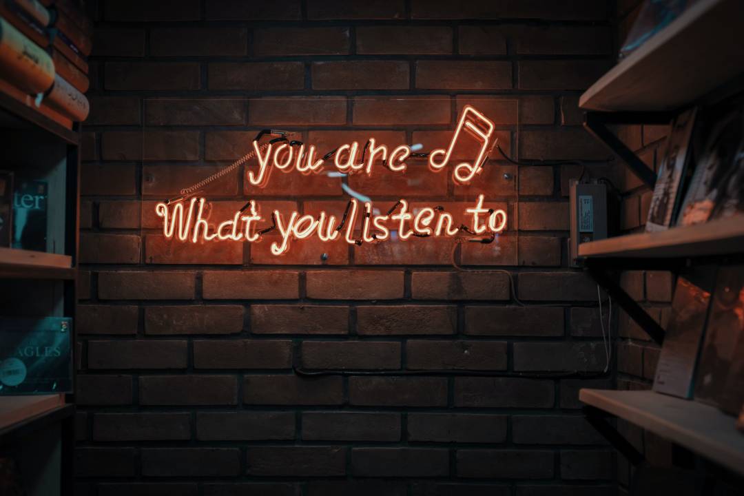 Orange Neon Sign On A Brick Wall Saying 'You Are What You Listen To'
