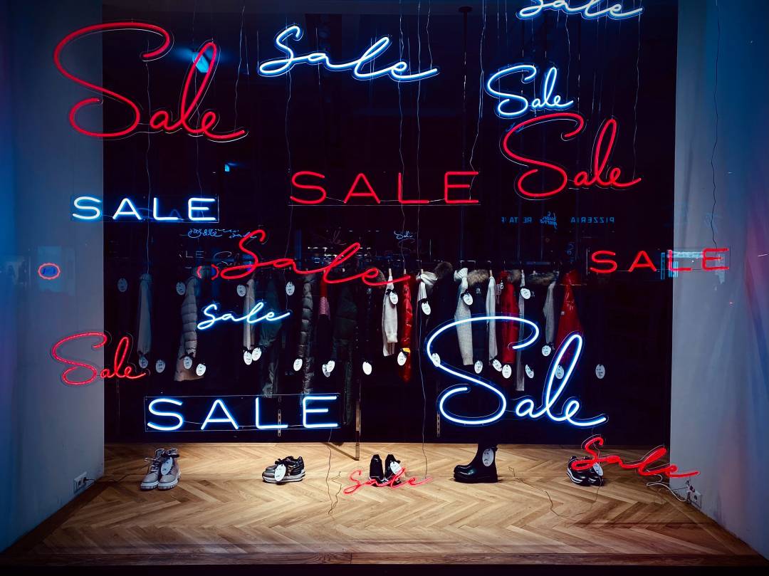 Shop window with clothes, shoes and multiple neon signs that say "Sale"