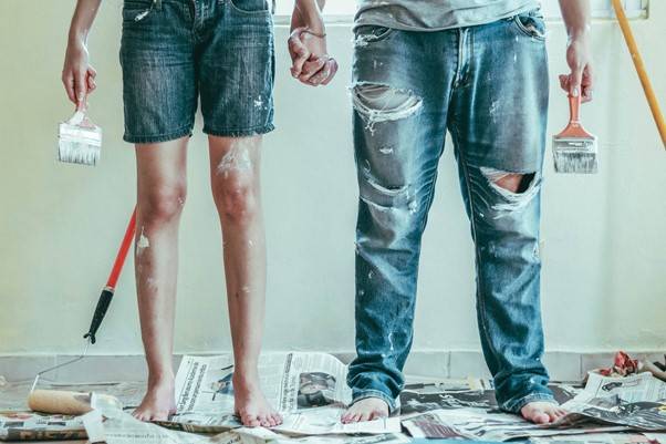 Couple dressed in paint-stained clothes, holding hands and a pair of paint brushes