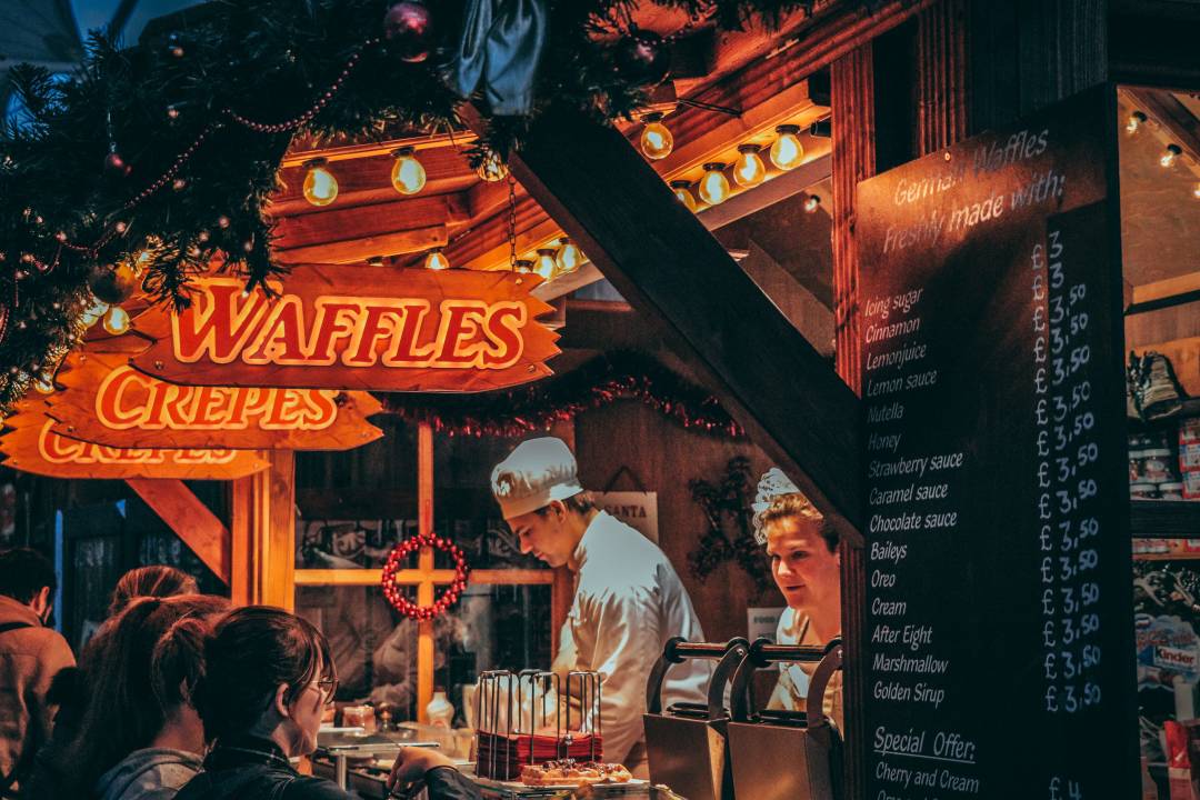 Winter market kiosk serving waffles and crepes with customers ordering food