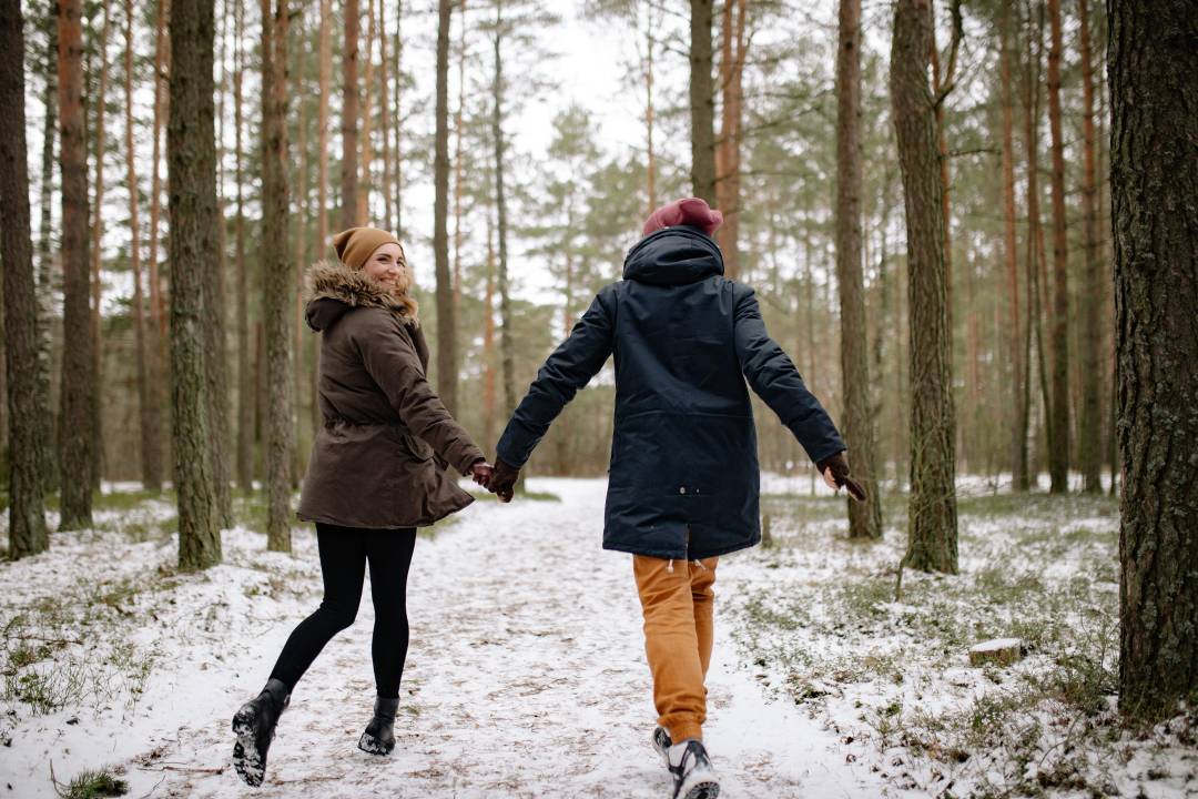 Couple holding hands and running in a winter forest with a dusting of snow