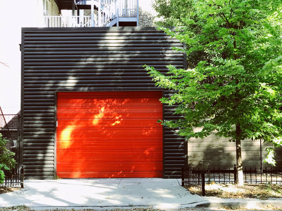 Red garage door on a residential street next to a tree