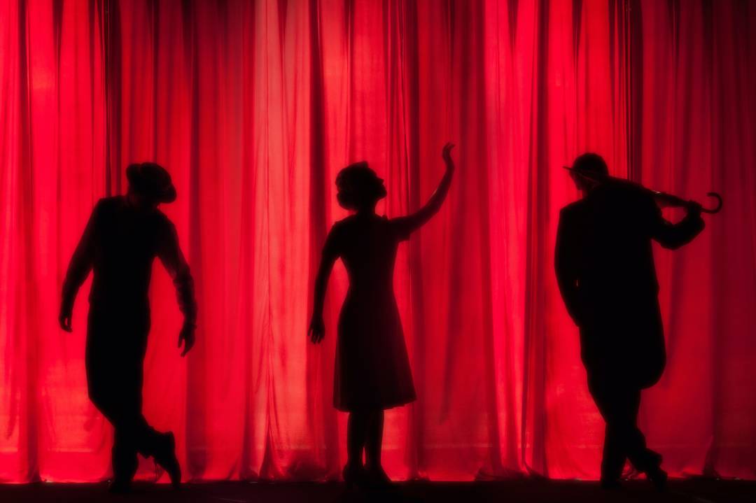 Silhouettes of people behind a red theatre curtain