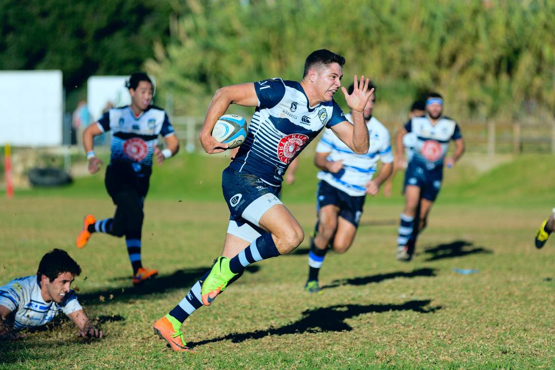 Player running with a rugby ball in his arms, being chased by other players