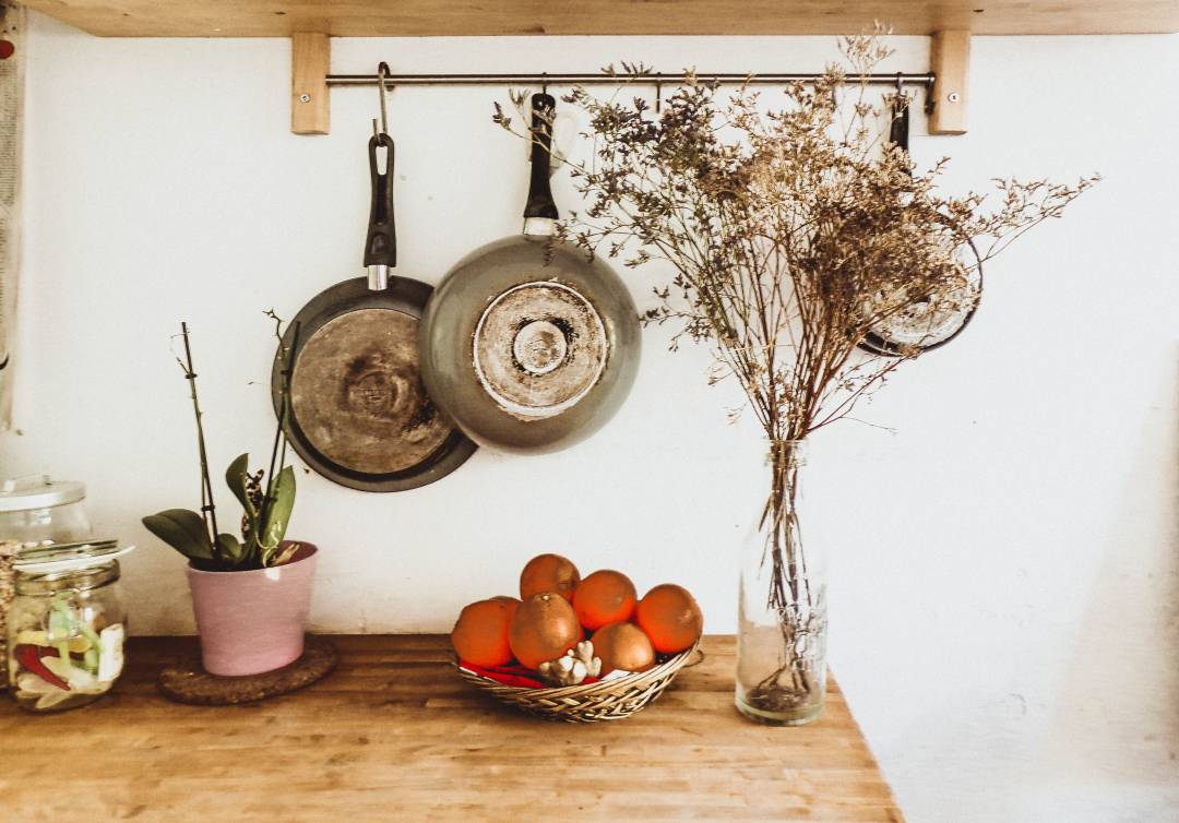 Pans Hung On The Wall Above A Work Surface With Flowers In A Vase