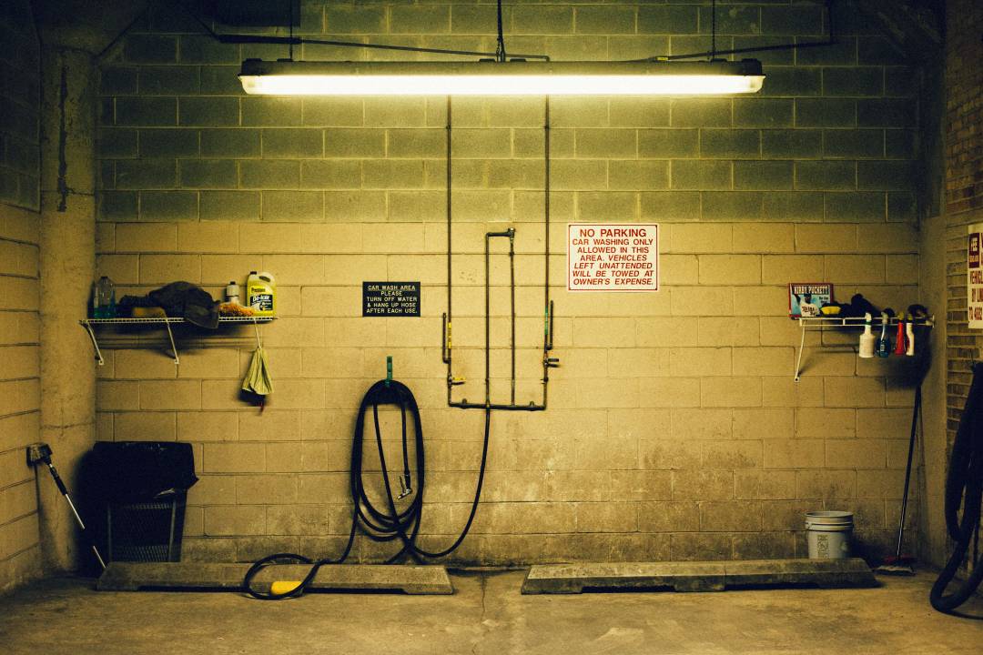 Inside of a garage wall, with hoses attached to it and a sign saying "No parking"