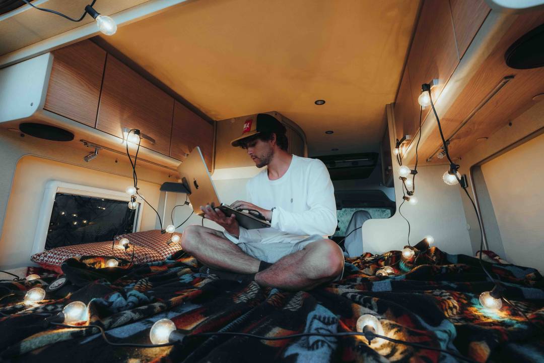 Man On Laptop Sat On Bed In Campervan
